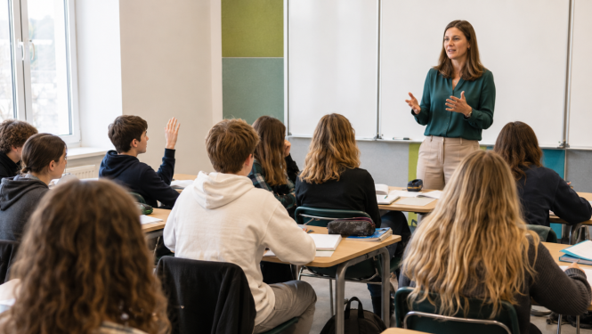 Skolotāja vada stundu 10. klases skolēniem, kuri sēž pie soliem un klausās klasē