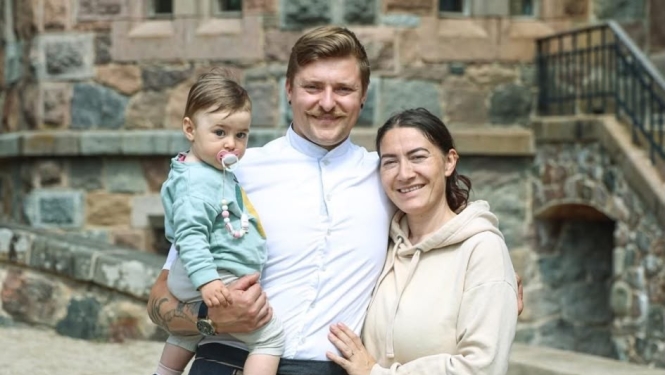 Šefpavārs Juris Latišenoks kopā ar dzīvesbiedri Lindu un mazo meitiņu pozē pie vēsturiskas akmens ēkas