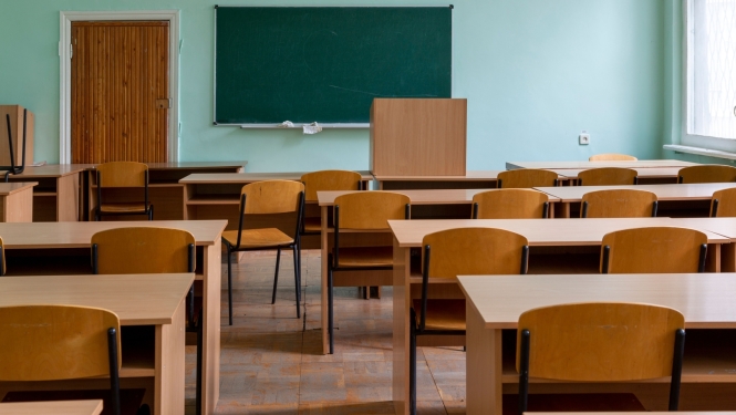 An empty classroom with desks, chairs, and a blackboard on the wall