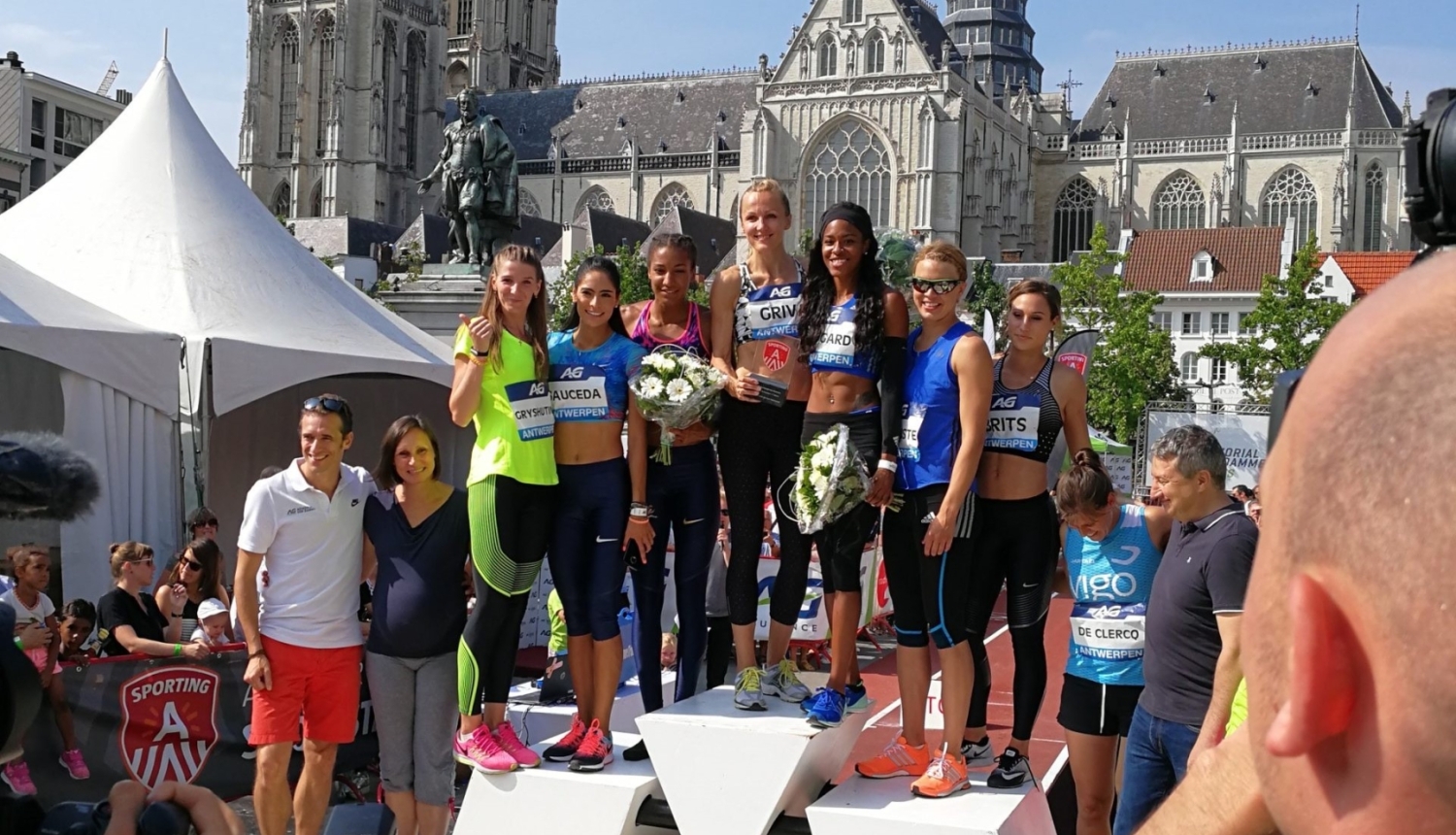 Sportistes stāv uz goda pjedestāla pēc sacensībām pilsētas laukumā pie vēsturiskas baznīcas